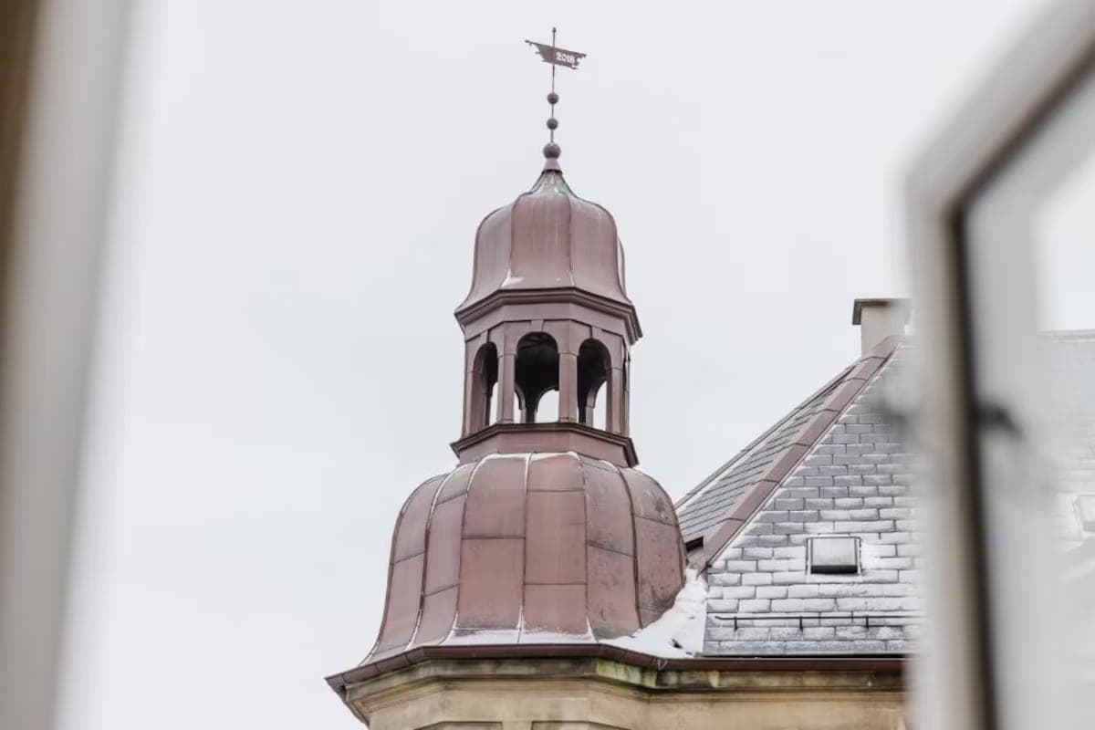 Copper tower and snowy rooftop framed by a window