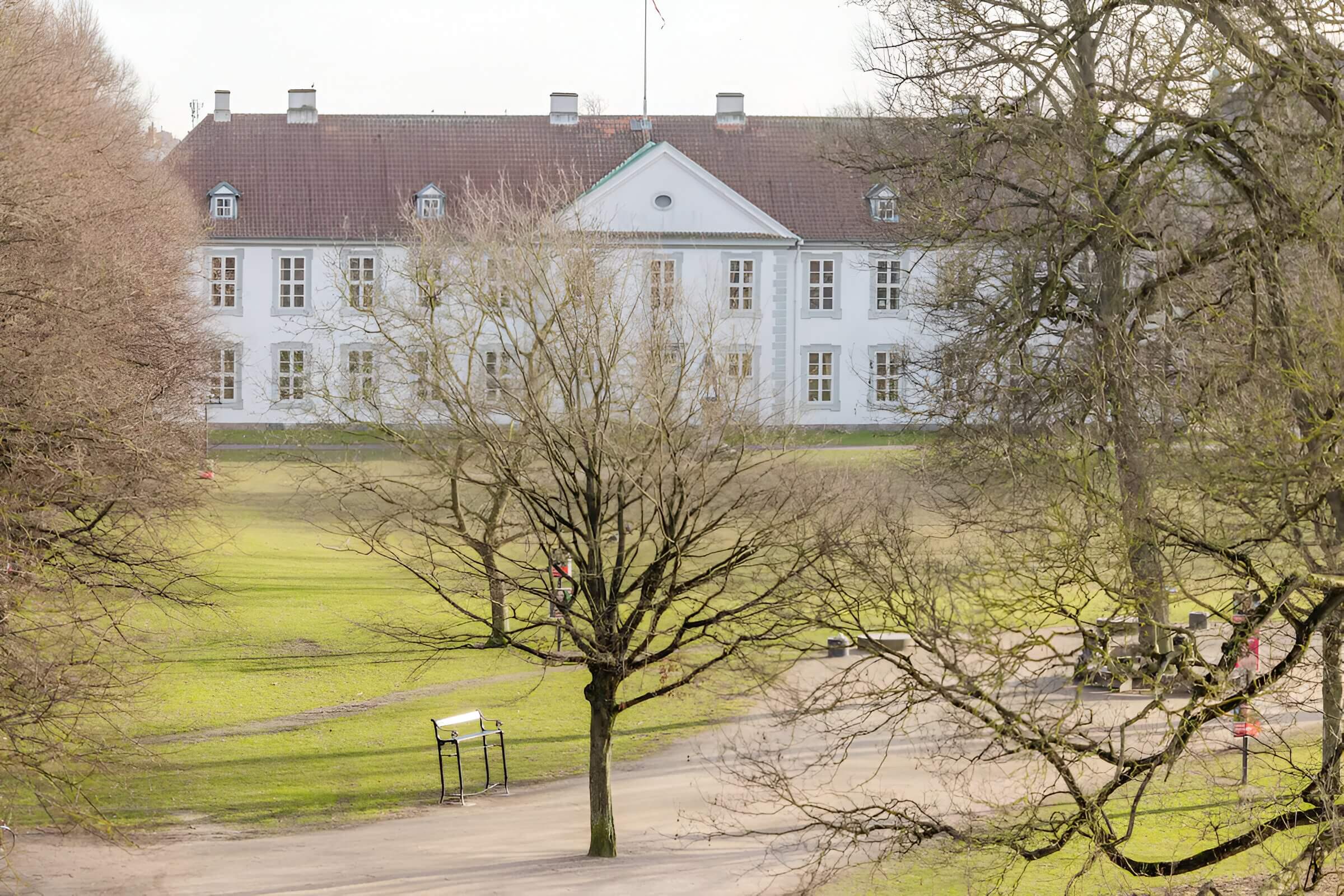 White historic building facing a park in Odense